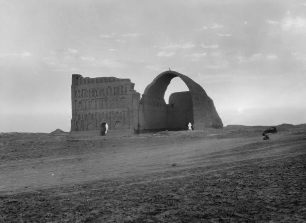 Black and white photo of the great brick arch of Ctesiphon standing in flat desert at sunset