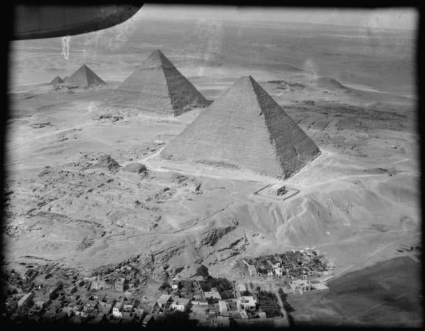 Black and white aerial photograph of the three Giza pyramids in a diagonal line above a village