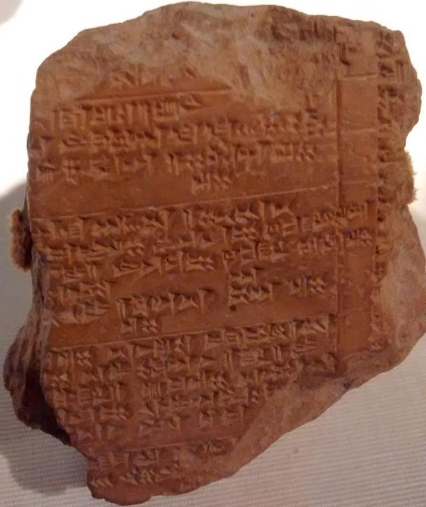 A brown baked clay tablet covered in rows of small wedge shaped cuneiform signs, displayed against a dark background