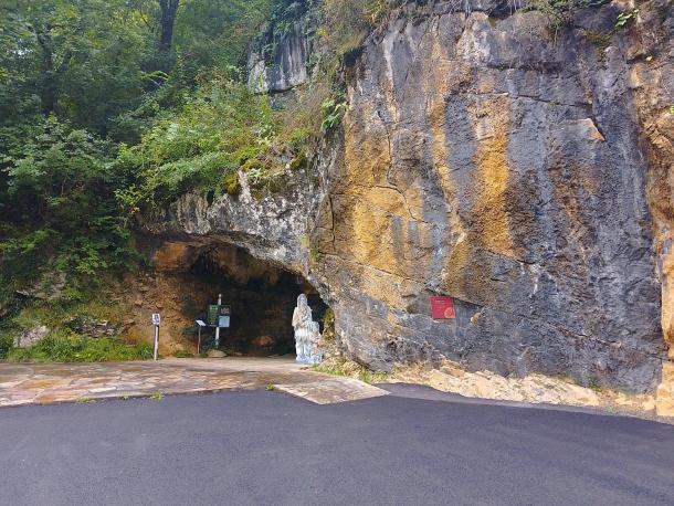 The rock face and arched entrance of the Isturitz and Oxocelhaya caves, with a paved road in front and trees above