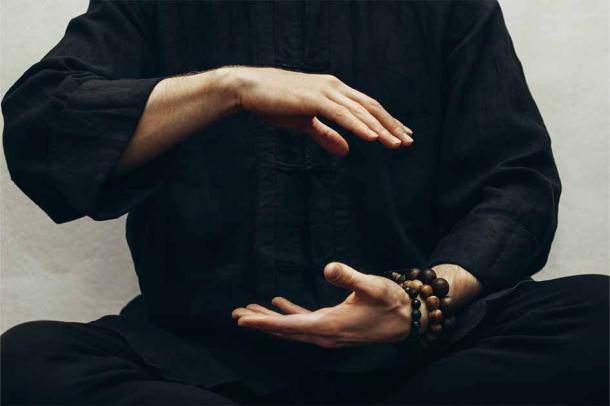A man in black shirt sitting and doing qigong with his hands directing his body's life energy or qi. Source: Anna / Adobe Stock