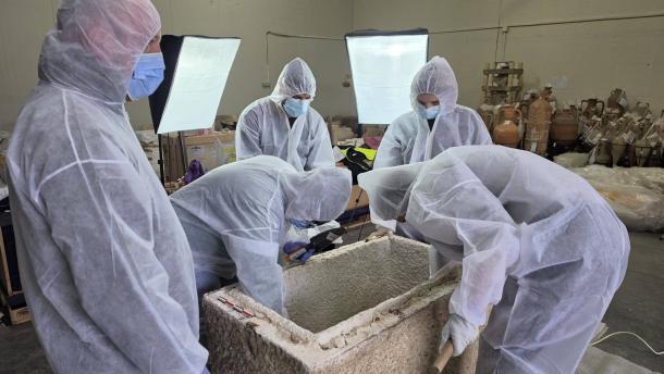 Museum specialists in white protective suits leaning over an open stone sarcophagus