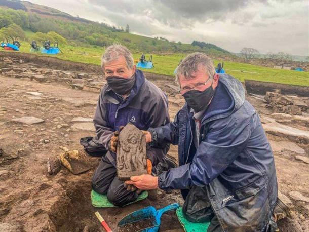 El último descubrimiento de Vindolanda, una tablilla de piedra tallada, es sostenida con orgullo por los voluntarios (Richie Milor y David Goldwater) que la encontraron, donde fue desenterrada. (Fideicomiso Vindolanda)