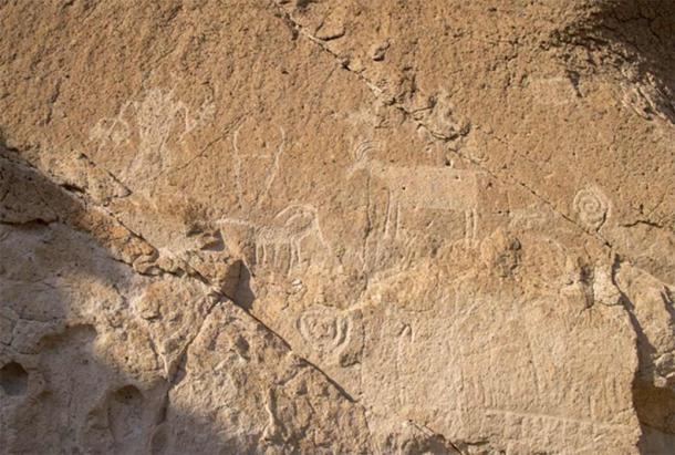A humanoid figure holds a ceremonial staff and basket in the upper left, while stylized sheep are framed by a pair of spirals; Fremont Indian State Park. (Photo © John Lundwall)