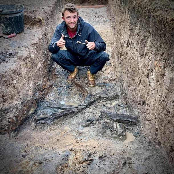 A Dig Venture team member squatting before the waterlogged timber structure of the ancient castle. (Dig Ventures)