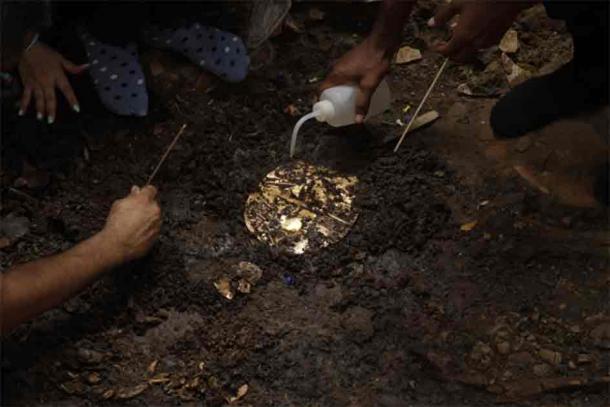 A gold breast plate being carefully removed from the earth. (Panama Ministry of Culture)