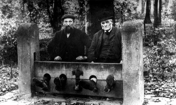 The punishment for Christmas cheer under Cromwell could be time spent in the stocks. Men in the village stocks as punishment, 1900 (Public Domain)