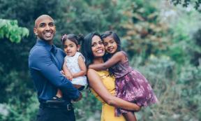 Indian family standing and smiling holding their kids in the park. Source: kristineldridge/Adobe Stock