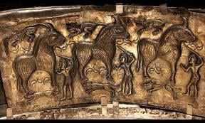 A panel from the Gundestrup Cauldron depicts three warriors sacrificing three bulls. The scene also features three hunting dogs and three felines, possibly leopards. 