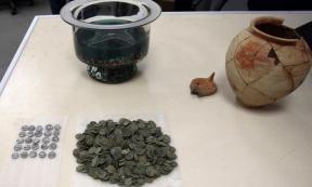 The ancient Roman coins, dating to the 1st century AD alongside the clay vessel in which they were found; the owner’s name is inscribed on the vessel. 
